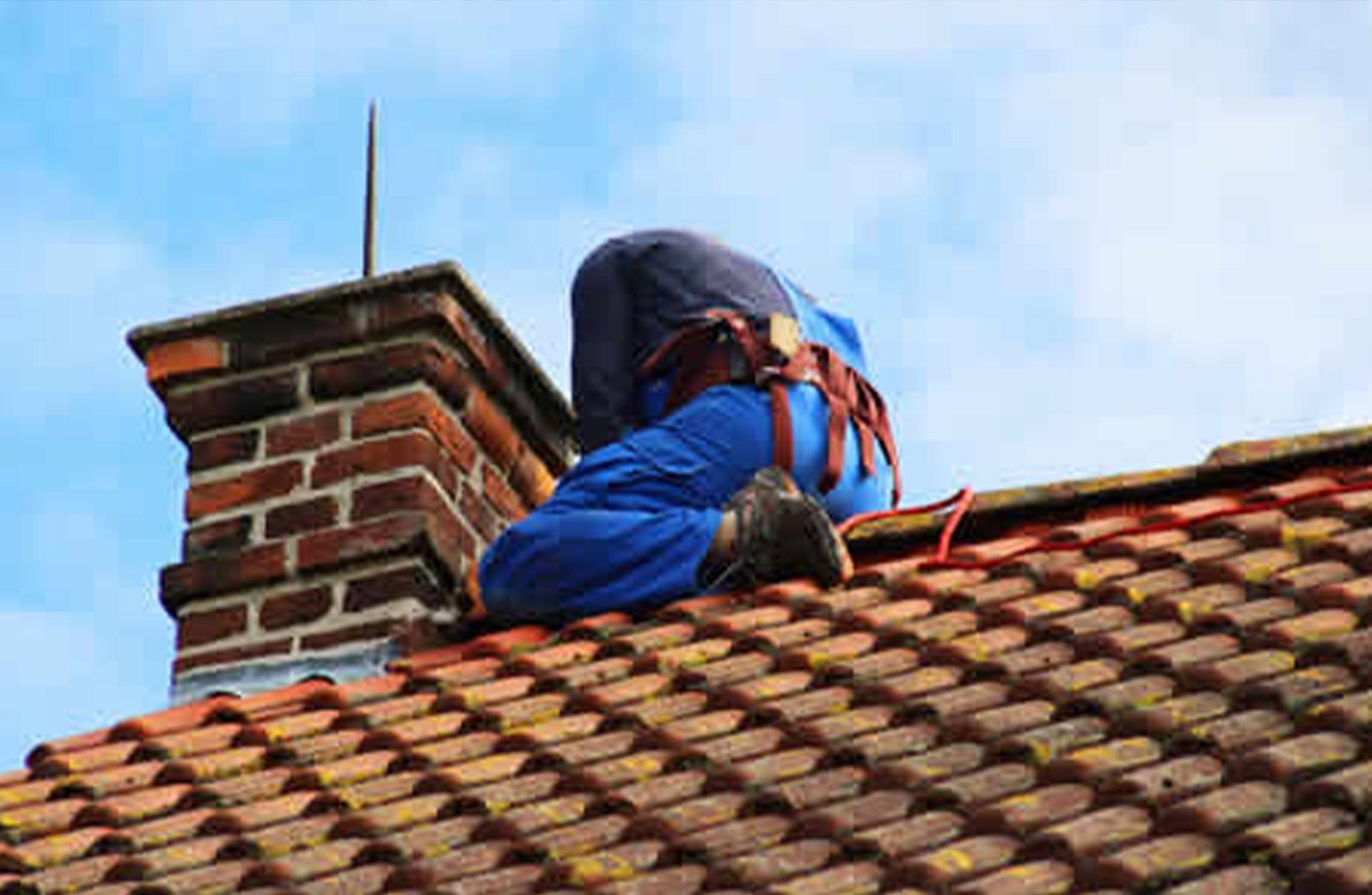 A man is sitting on top of a tiled roof next to a chimney.
