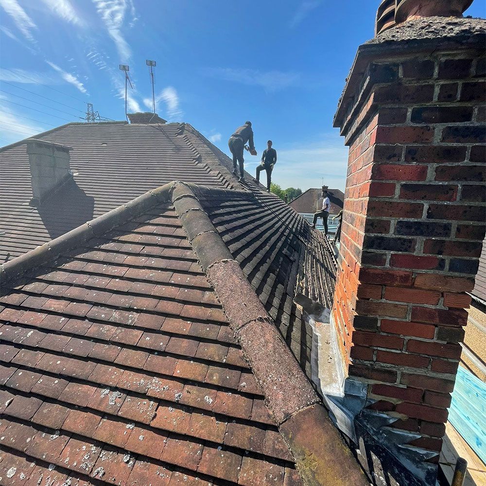A man is standing on top of a roof next to a chimney.