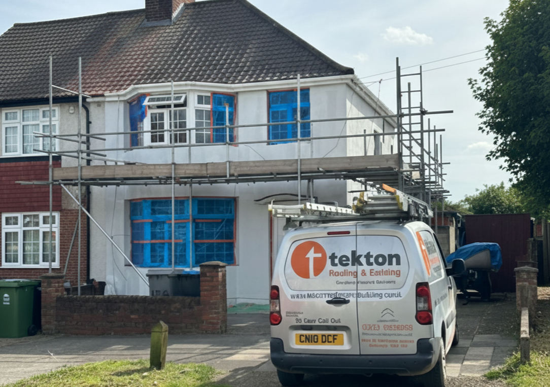 House in Isleworth under renovation with scaffolding, blue-taped windows, and a Tekton Roofing and Building van parked out front.