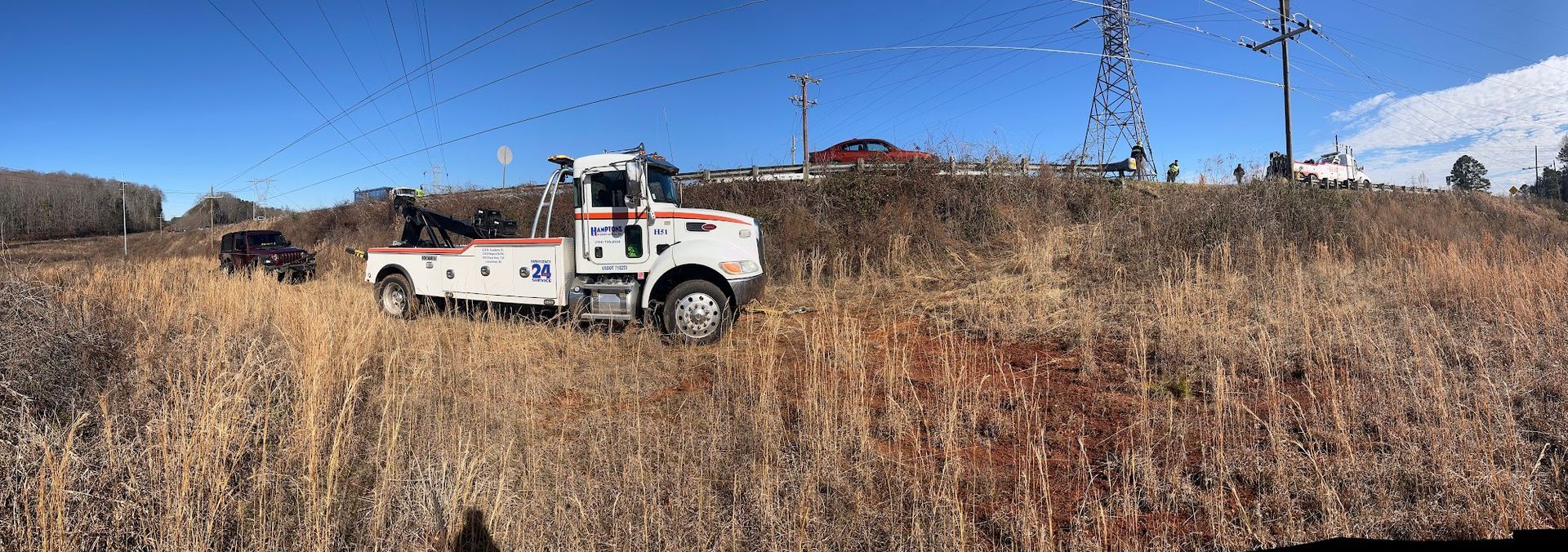 A white tow truck is parked in a field of tall, dried grass. The sky is blue.