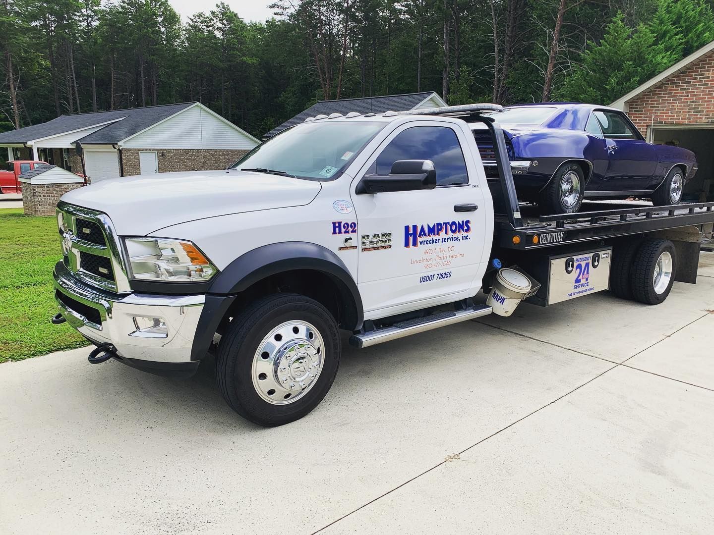 White tow truck with a blue classic car on the bed, parked on a driveway.