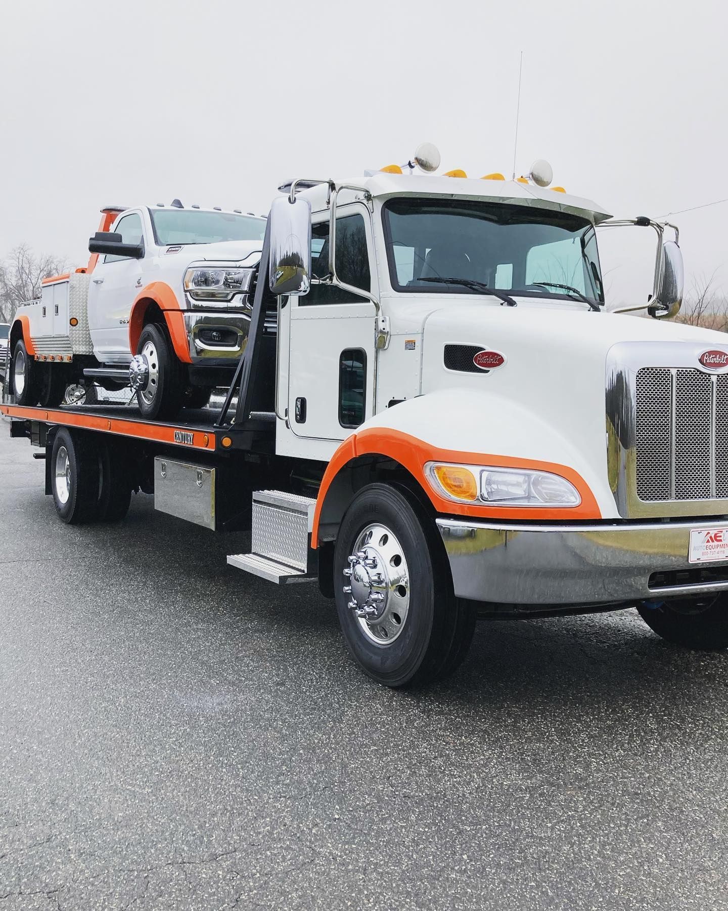 Tow truck with a white pickup truck on its flatbed, on a road. The tow truck is white with orange accents.