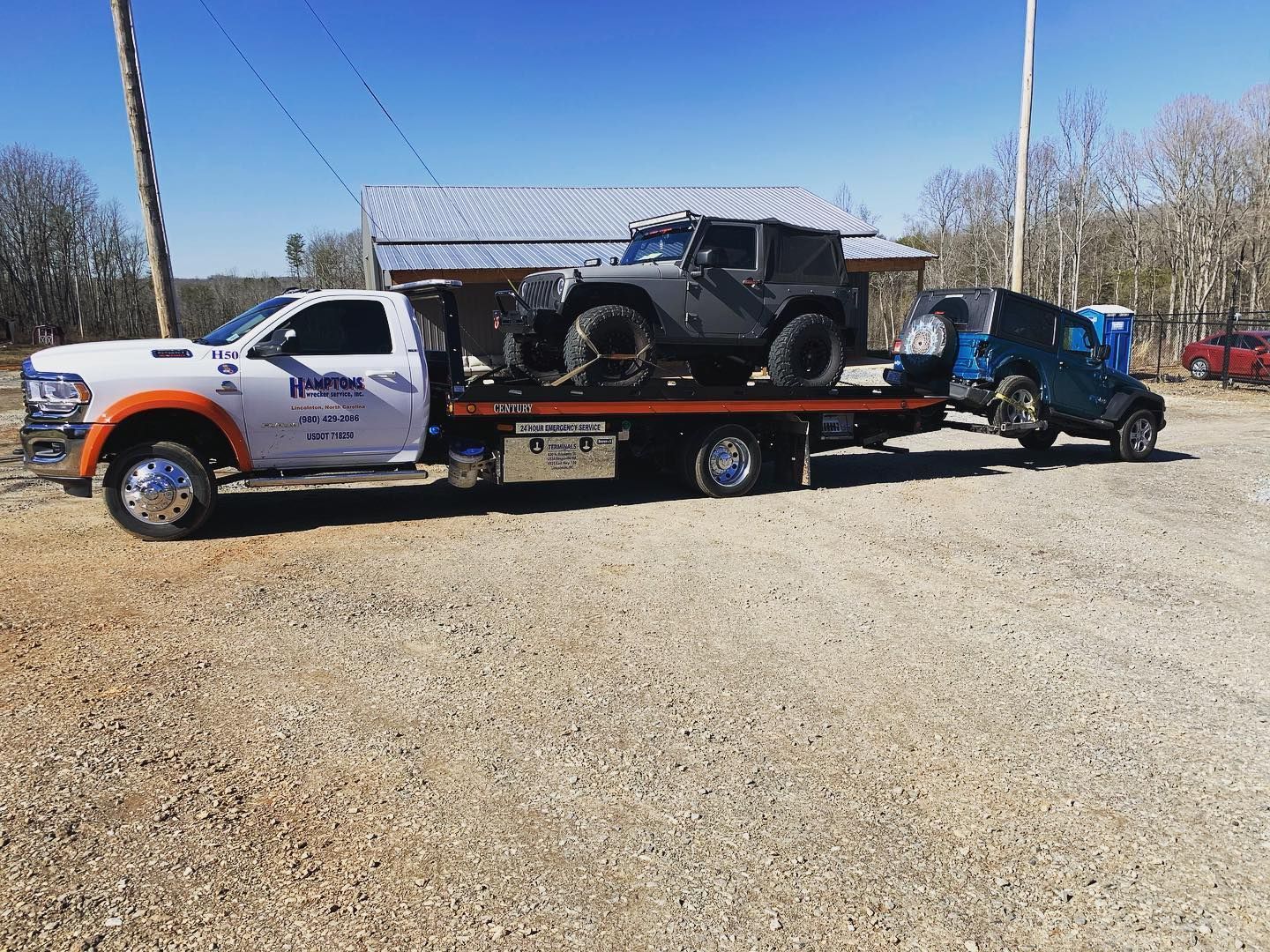 Tow truck carrying two jeeps on a gravel lot. One jeep is on the flatbed, the other is attached to the rear.