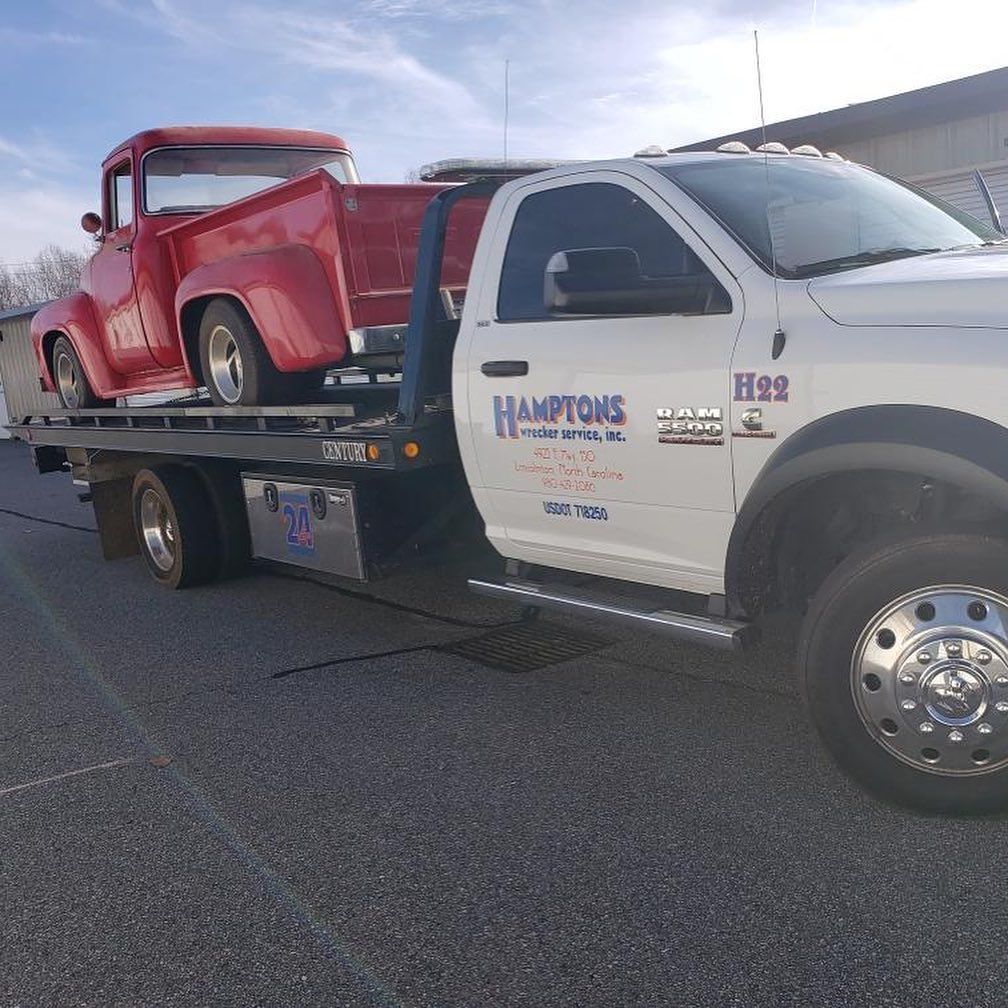 A red vintage pickup truck is being towed by a white tow truck labeled 