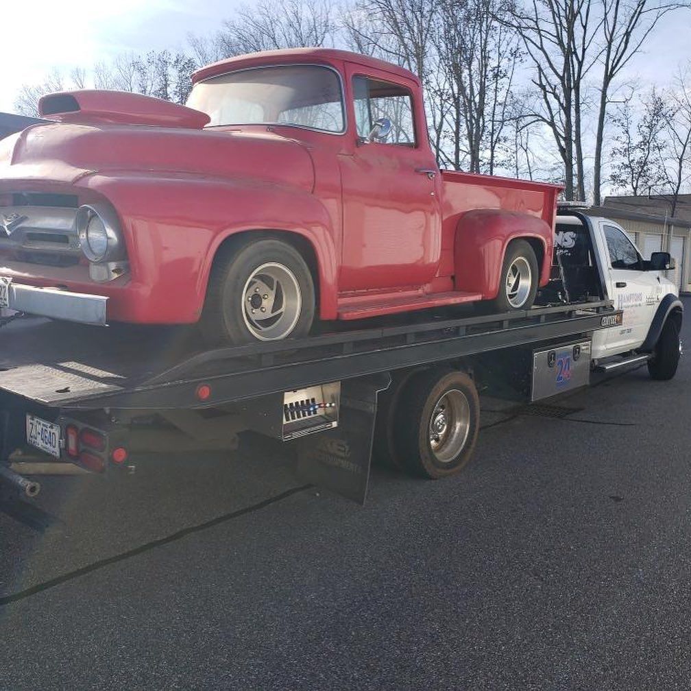 Red vintage pickup truck being transported on a flatbed tow truck.