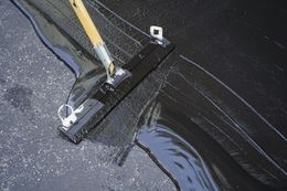 A broom cleaning black liquid spill on dark pavement.