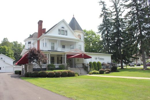 Gray building with a covered entrance, double doors, and windows. Two green bushes flank the entrance.
