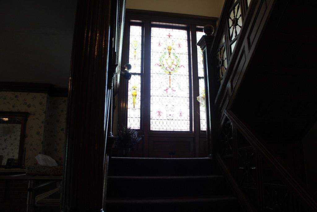 Dark interior staircase leads up to a stained glass door with bright sunlight filtering through.