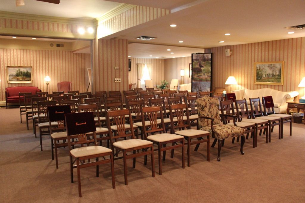 Interior of a funeral home chapel with rows of chairs, a red couch, and beige walls.