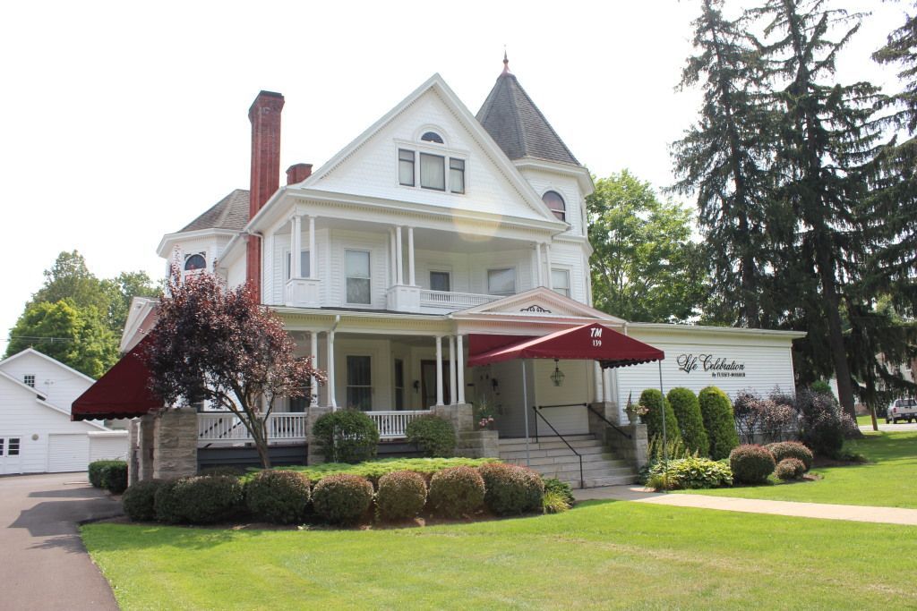 White Victorian house with a red awning over the porch entrance, surrounded by green grass and trees.