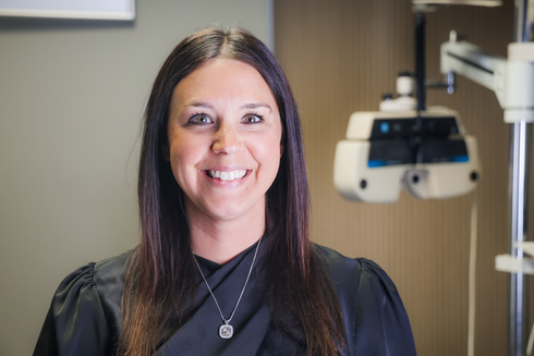 Smiling woman with dark hair in a teal top standing in a bright eyewear store