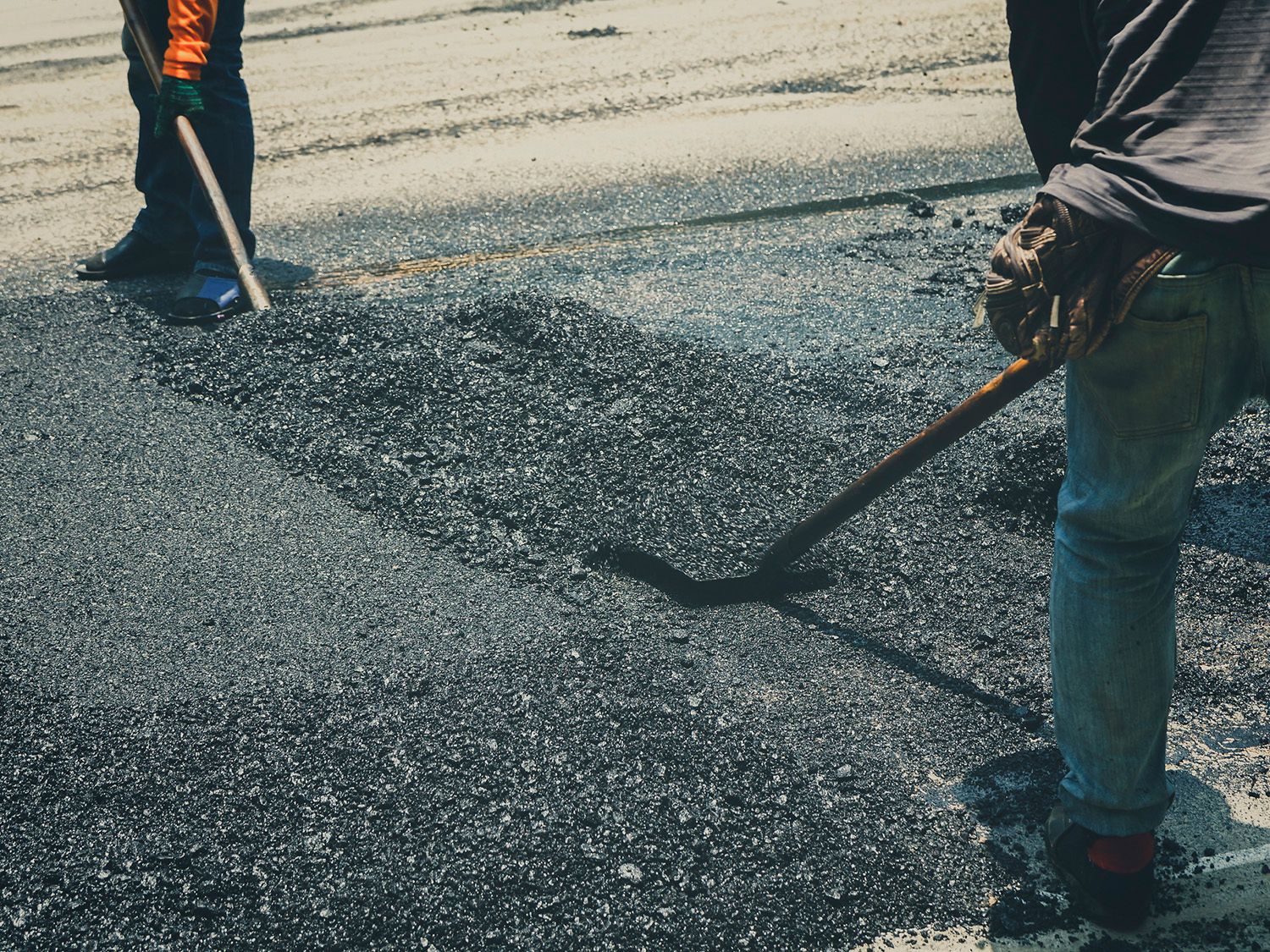 A man is using a rake to spread asphalt on the ground.