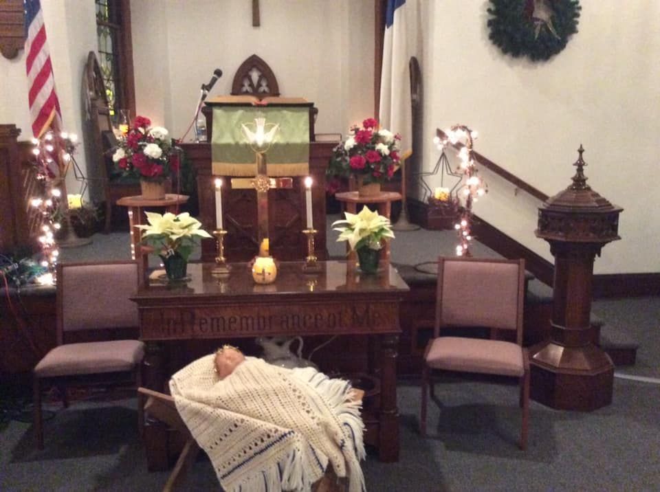Church altar decorated for Christmas with flowers, candles, and a nativity scene.
