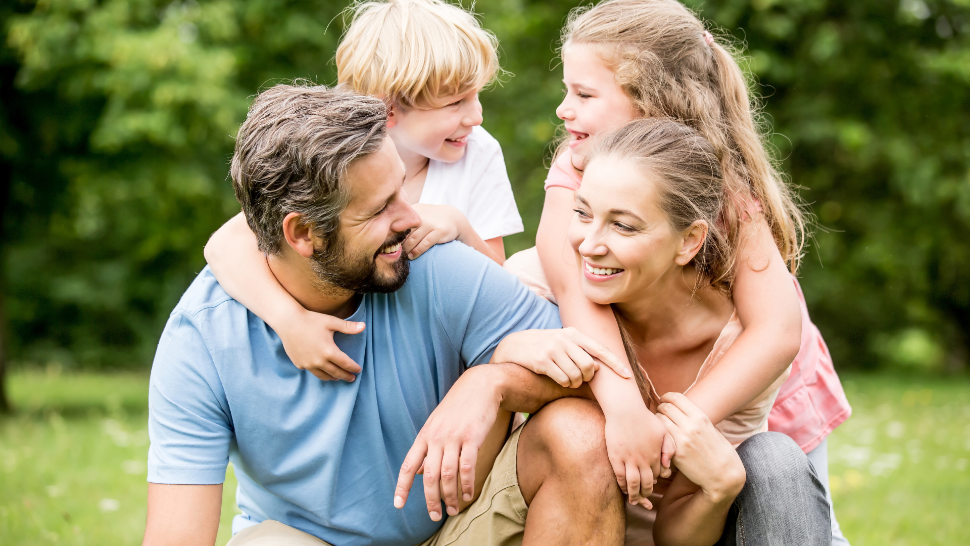 Family of four smiling, outdoors, with kids hugging their parents.