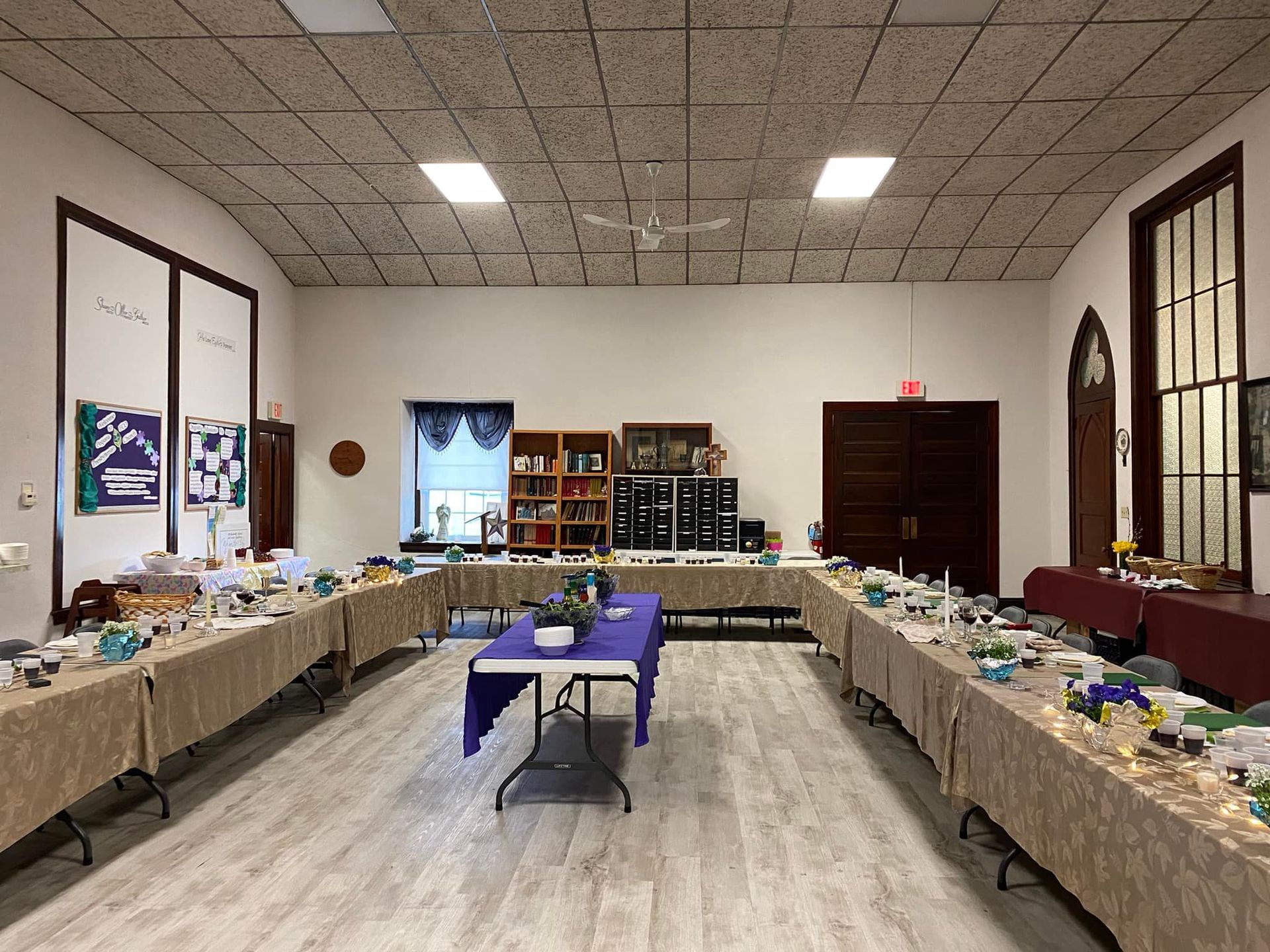 Long tables arranged in a U-shape, set for an event in a brightly lit hall.