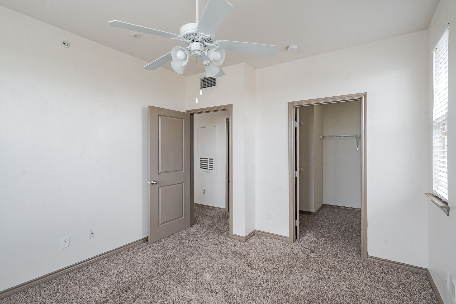 Empty bedroom with neutral walls, beige doors, a ceiling fan, and a closet.