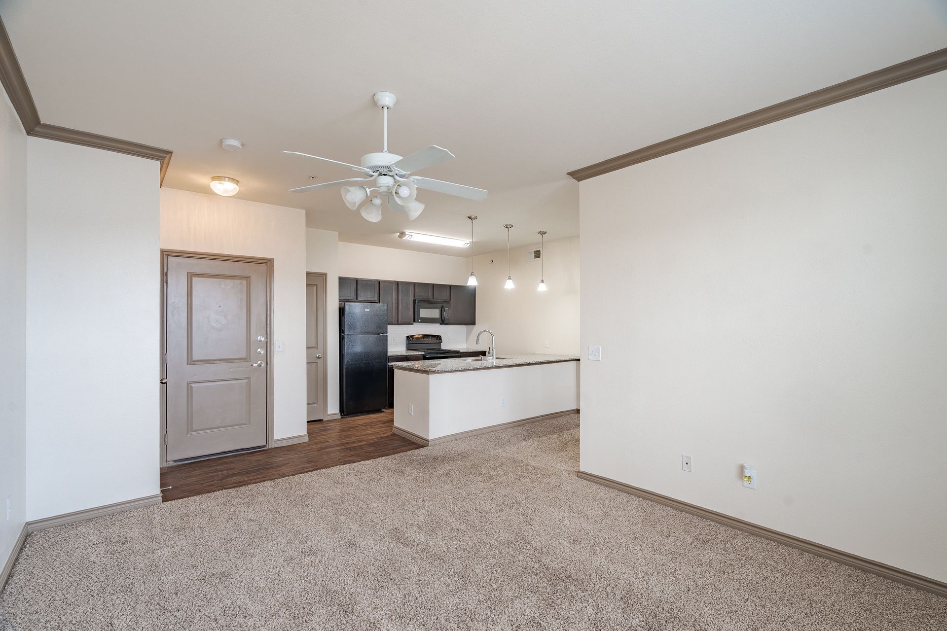 Open-concept living area with kitchen island, black appliances, and ceiling fan.