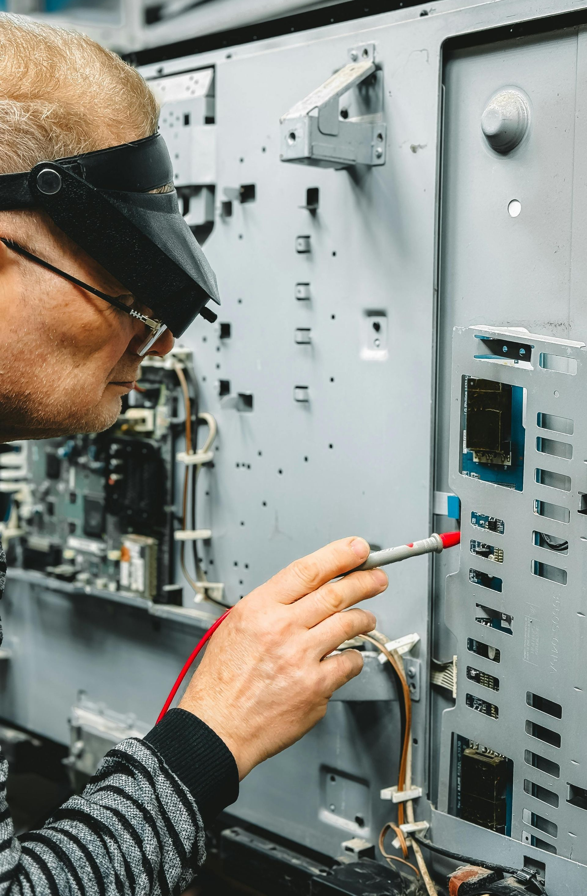 Man in glasses and magnifying visor tests electrical equipment with a probe.