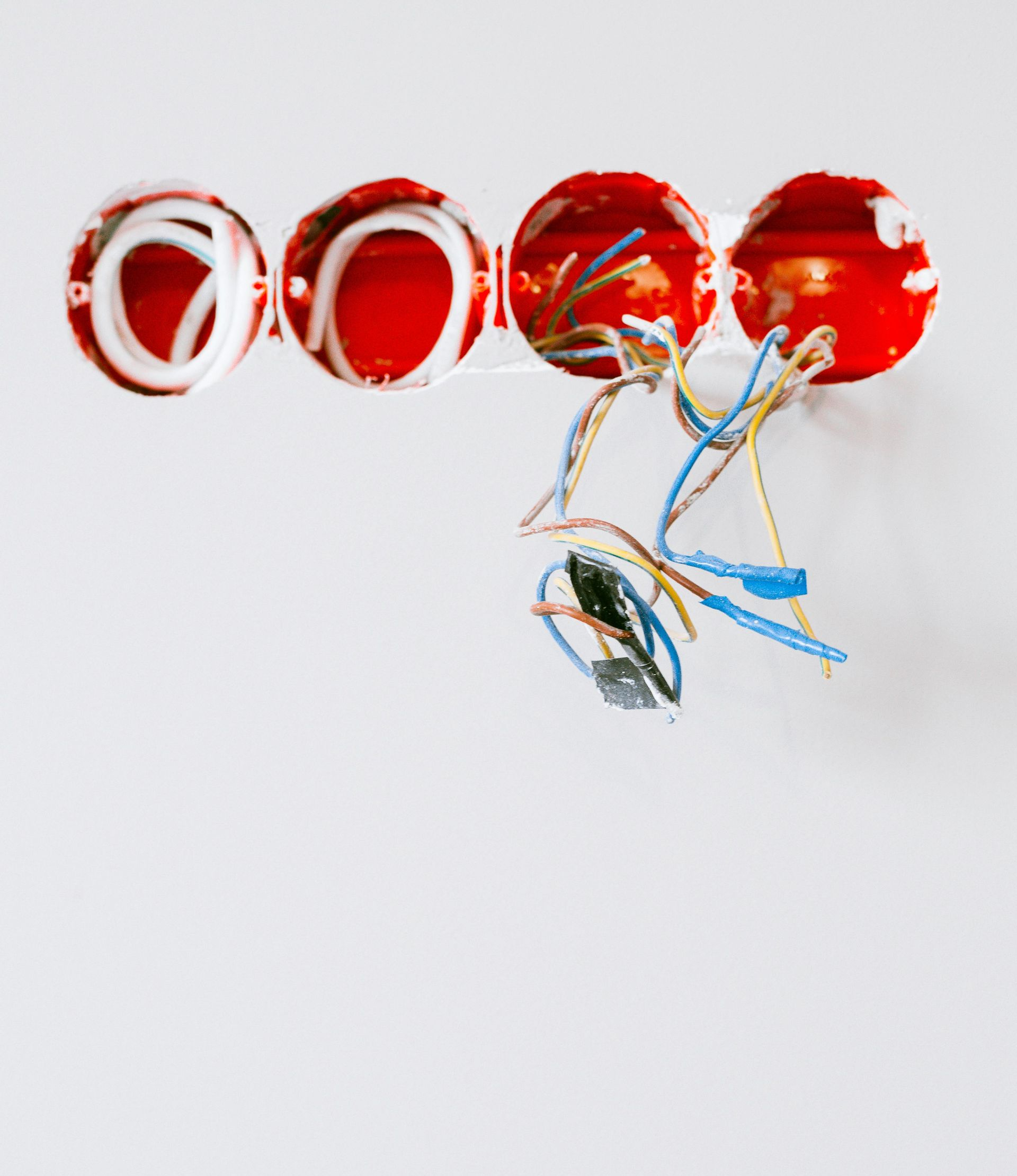 Four red electrical boxes in a white wall, with exposed wires in a construction setting.