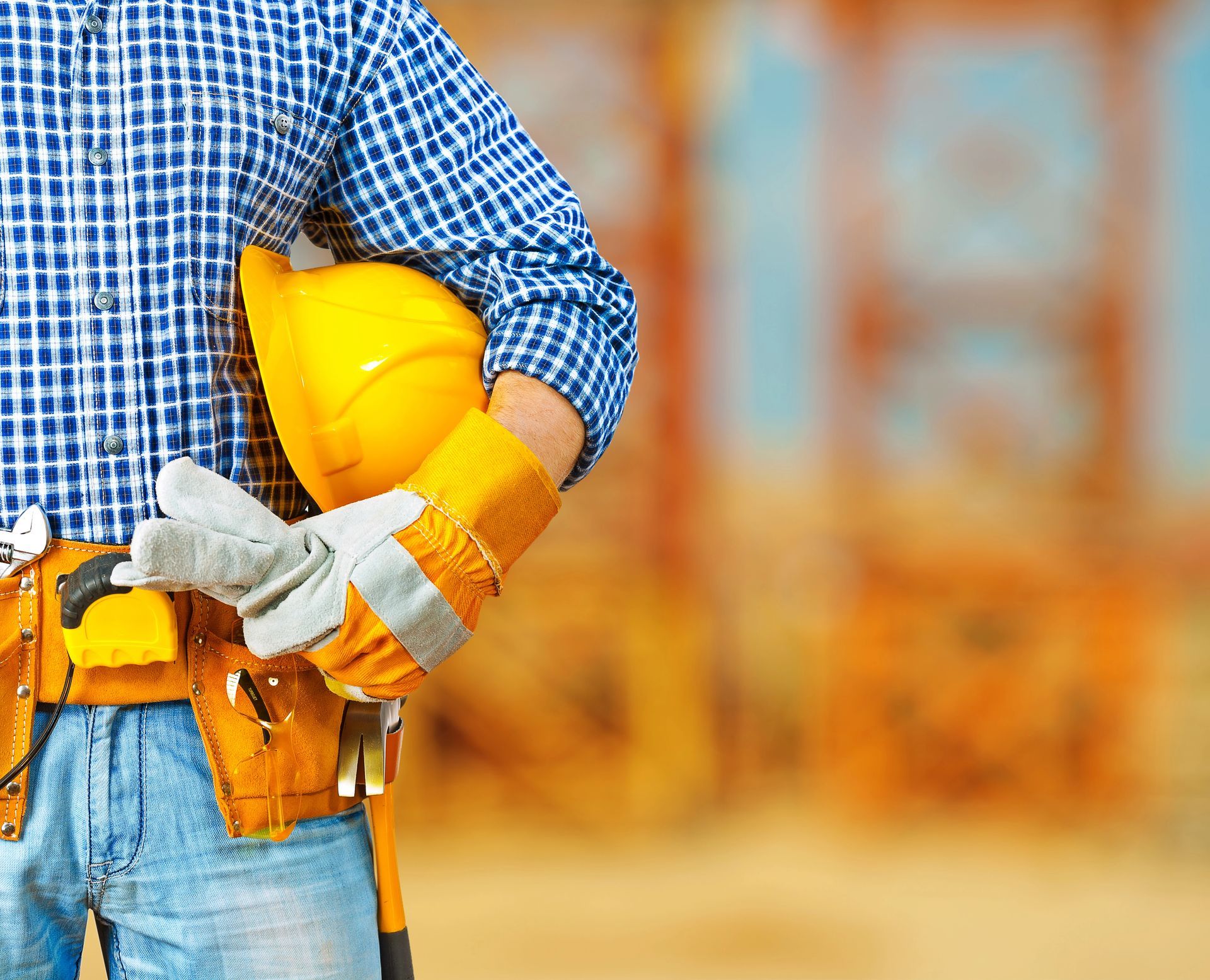 Operaio edile con camicia a quadri blu, elmetto giallo e attrezzi in un cantiere.