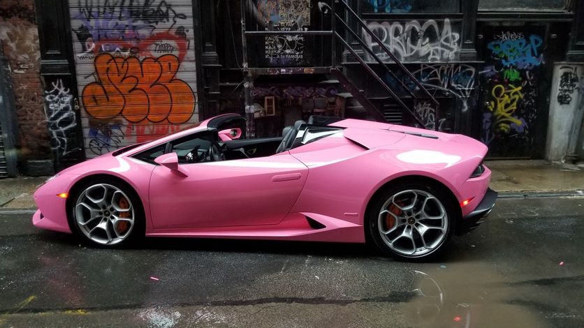 Pink Lamborghini convertible parked in an alley with graffiti-covered walls.