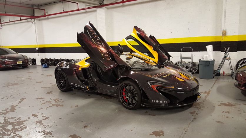 Black McLaren sports car with butterfly doors open in a garage, featuring yellow accents.