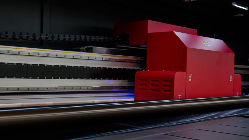 Large red industrial printer in a dark room, printing on a flat surface.