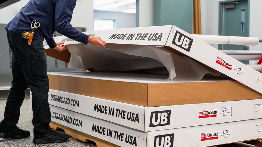 Person opening a cardboard box labeled "Made in the USA." Boxes are stacked. Inside, the item is wrapped.