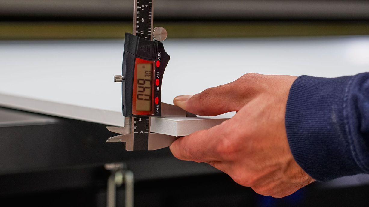 Person measuring the thickness of a white material with digital calipers; reading shows 0.49.