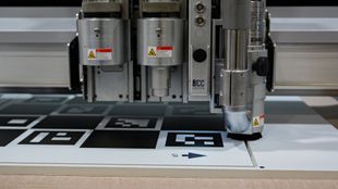 Close-up of a machine cutting a white surface with black markers. Industrial setting.