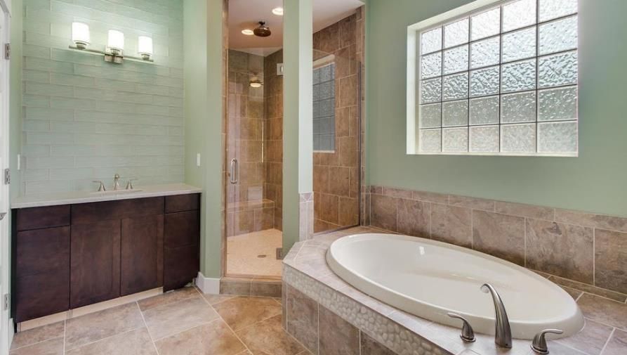 Bathroom with tub, shower, and vanity. Green walls, brown cabinets and tile, and a glass block window.
