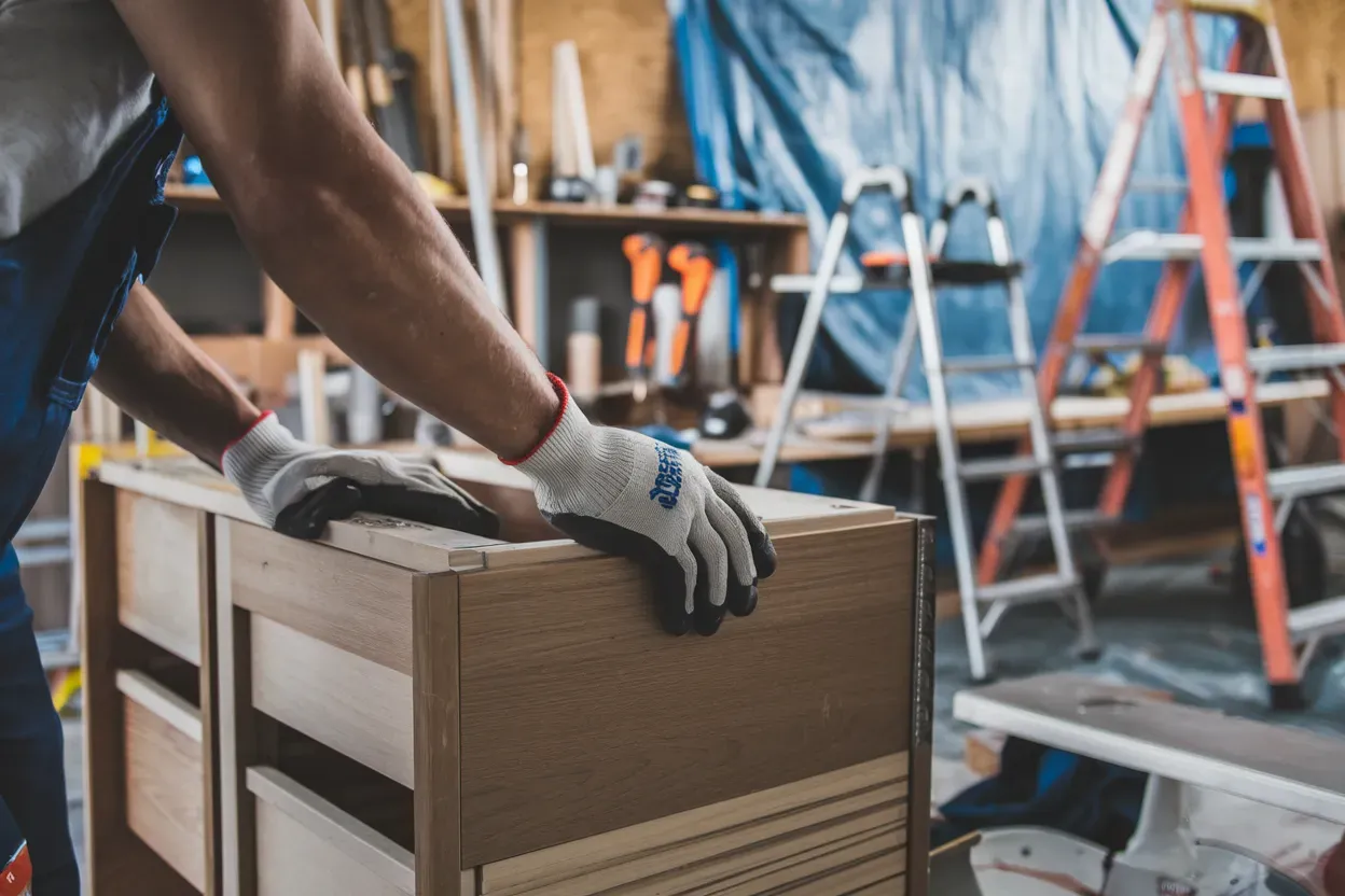 Person wearing gloves working on a wooden cabinet in a workshop.