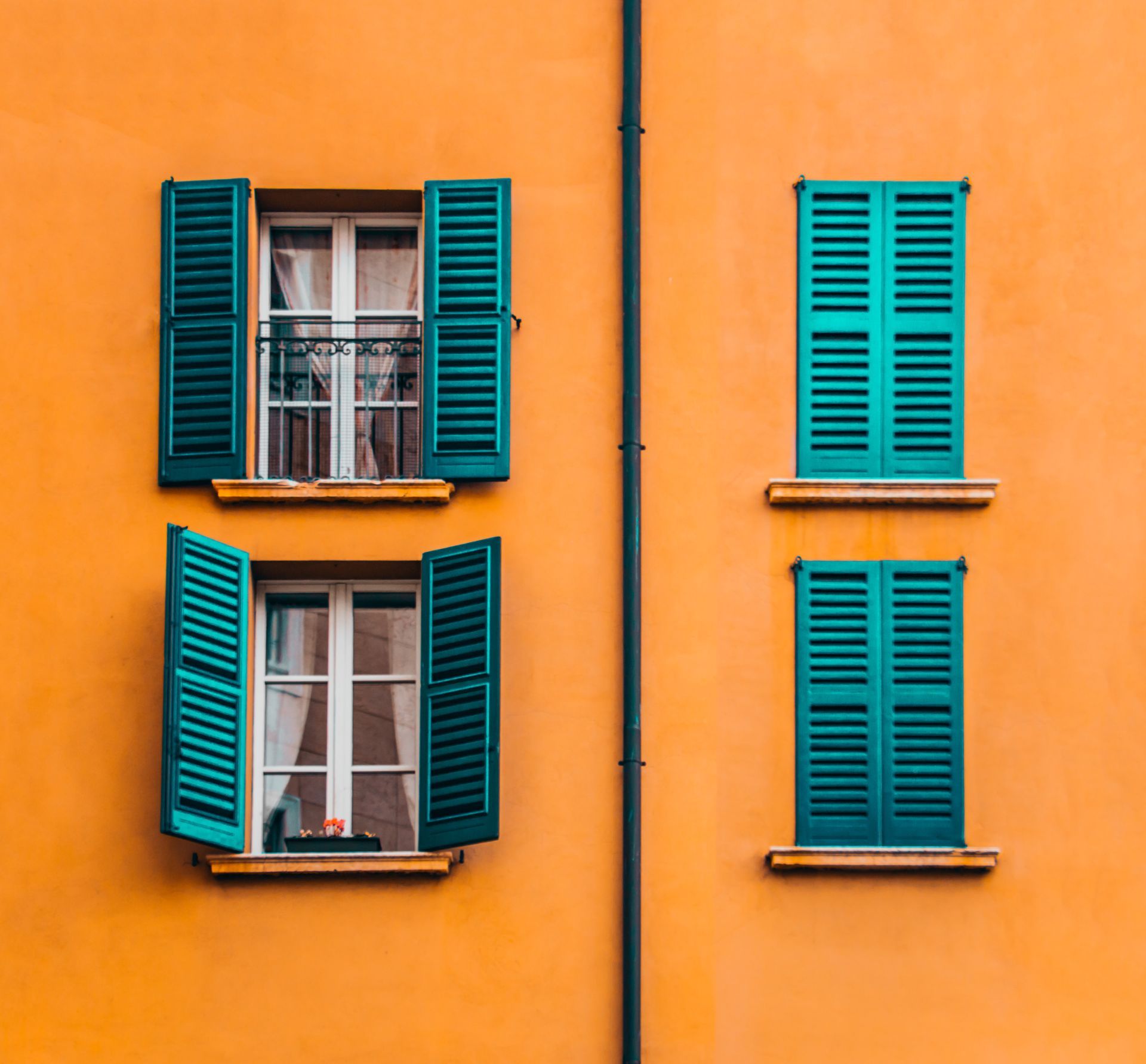 Two windows with green shutters on an orange building.