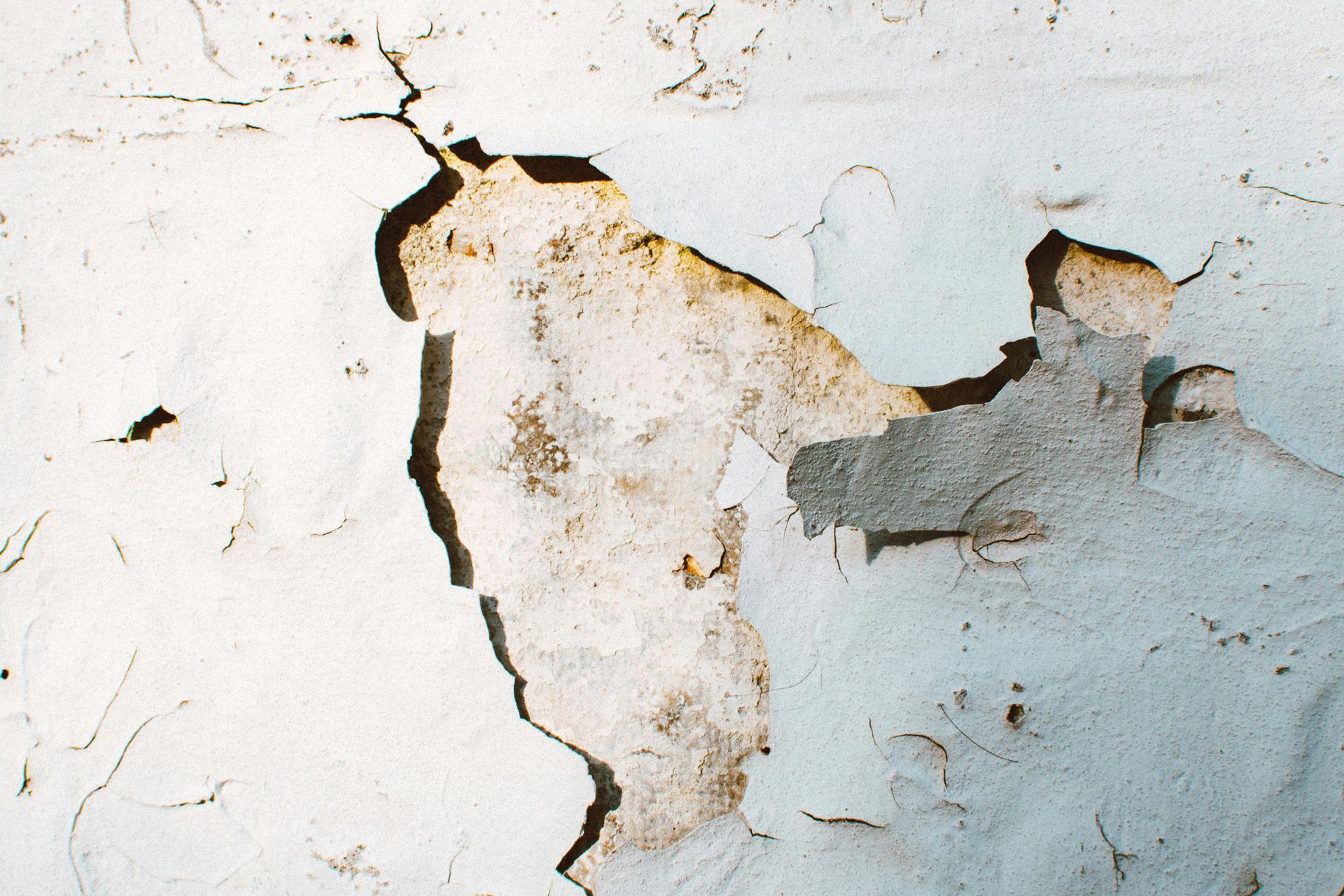 Cracked and peeling white paint on a wall, revealing underlying layers of different colors.