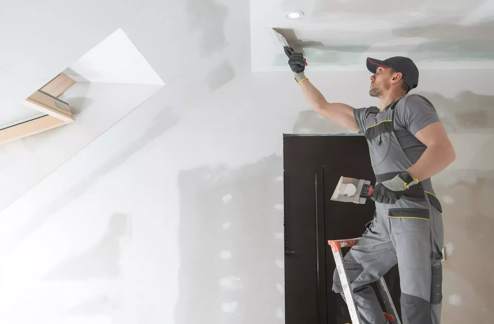 A man is standing on a ladder and plastering a ceiling.