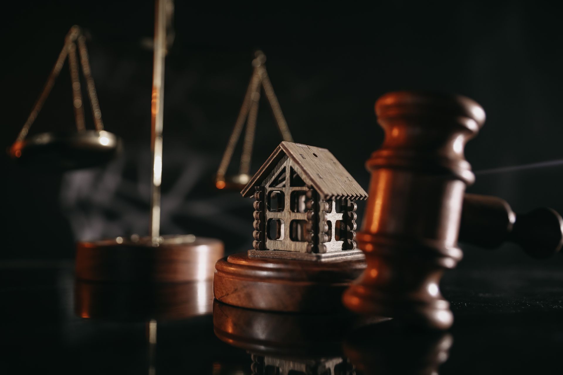 Scales of justice, gavel, and miniature house on a dark surface, symbolizing legal and real estate.