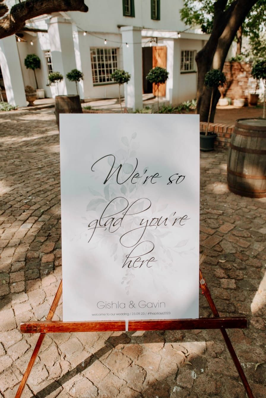 A welcome sign is sitting on a wooden easel in front of a building.