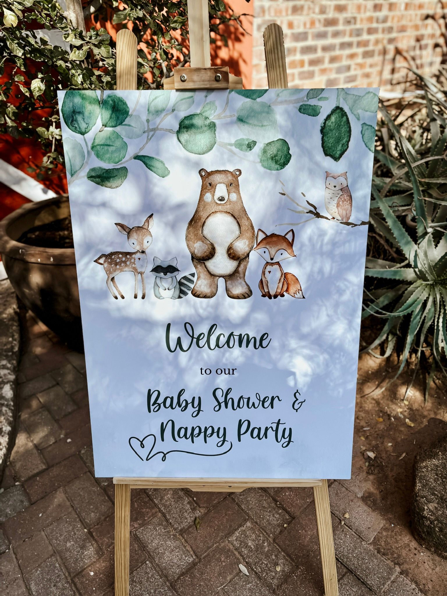 A welcome sign for a baby shower is sitting on a wooden easel.
