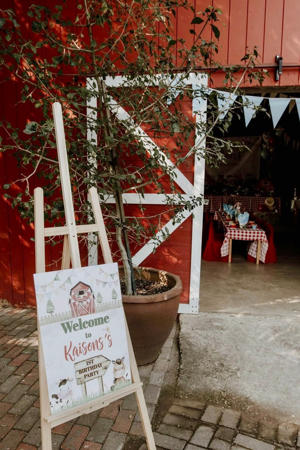 A wooden easel with a sign on it in front of a red barn.