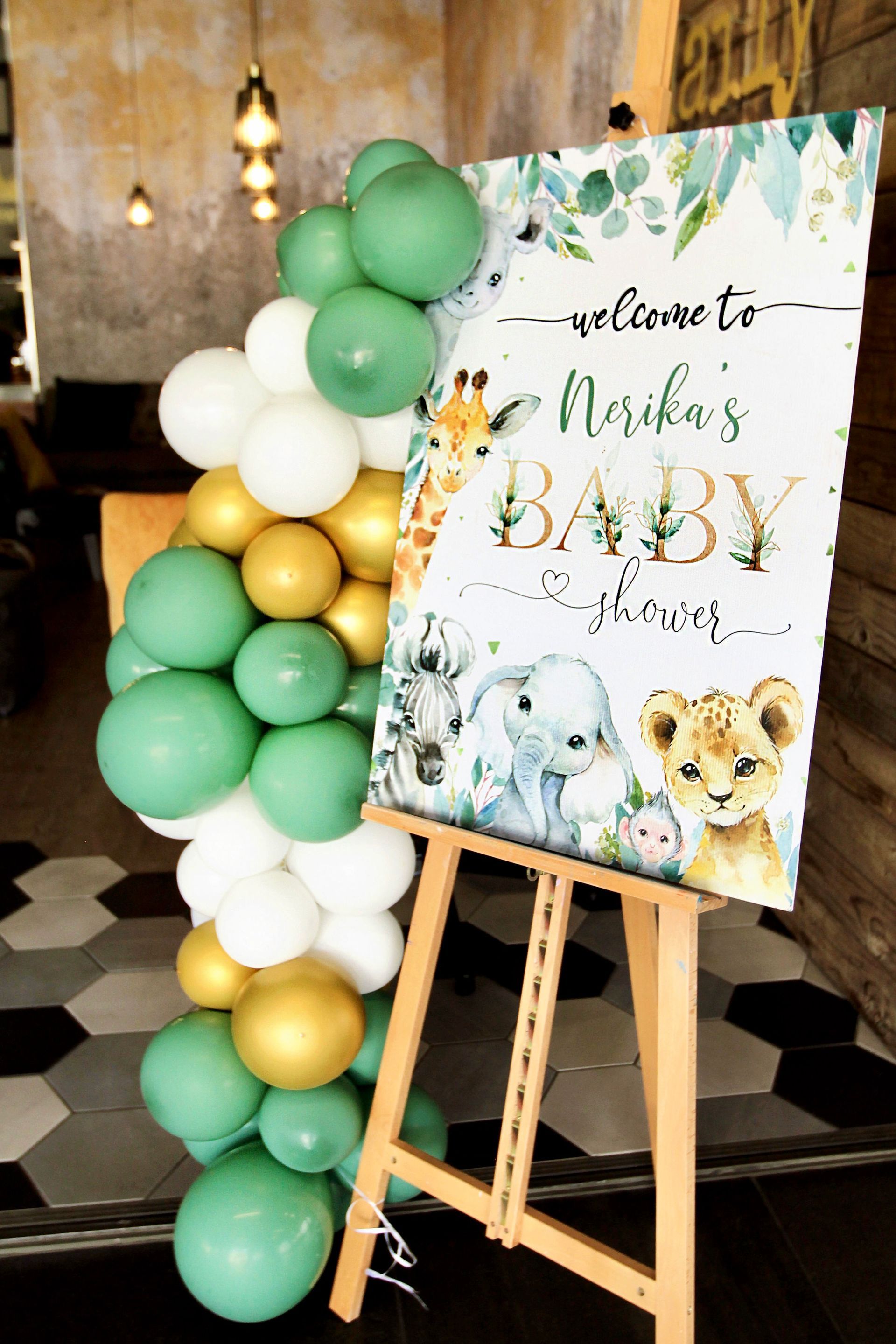 A baby shower sign is sitting on a wooden easel surrounded by balloons.