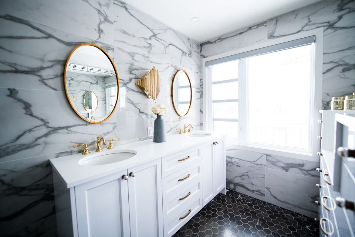black tiled bathroom with a white sink and countertop, gold framed mirrors with window with sunlight