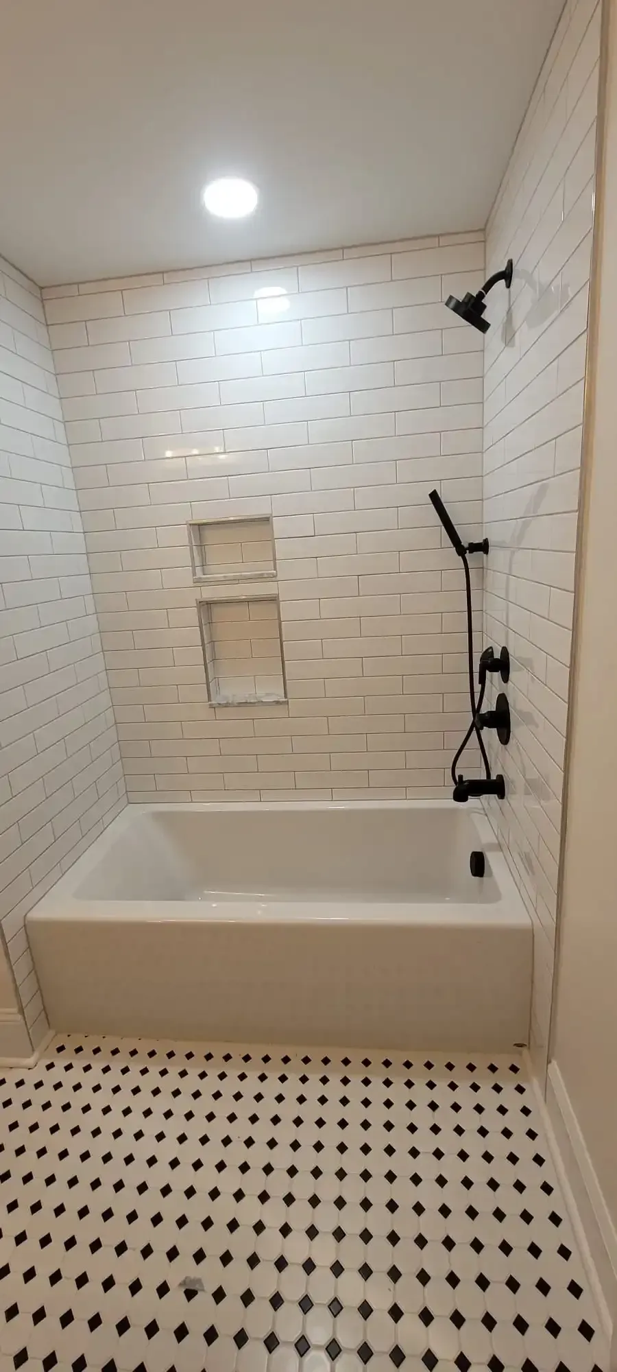 A bathroom with a bathtub , shower , and black and white tile floor.