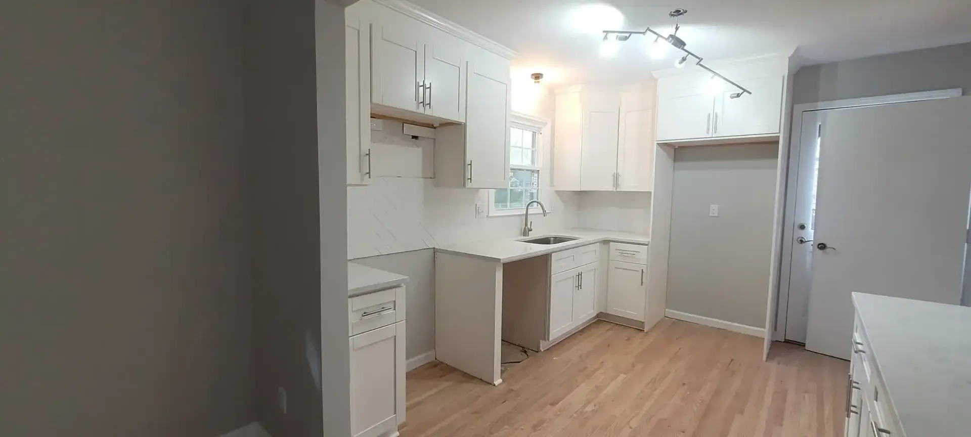 An empty kitchen with white cabinets and hardwood floors.
