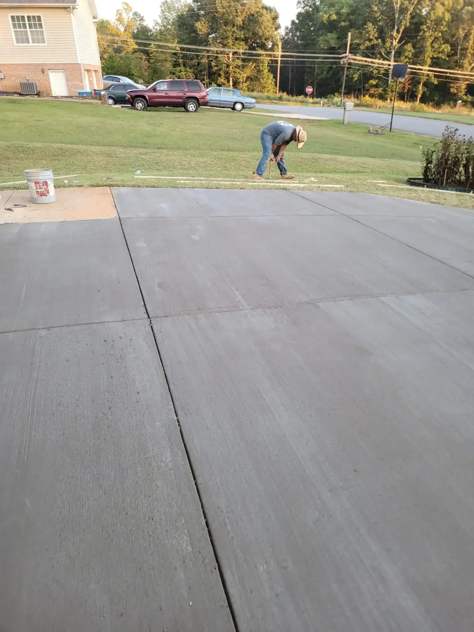 A man is kneeling down on a concrete driveway.