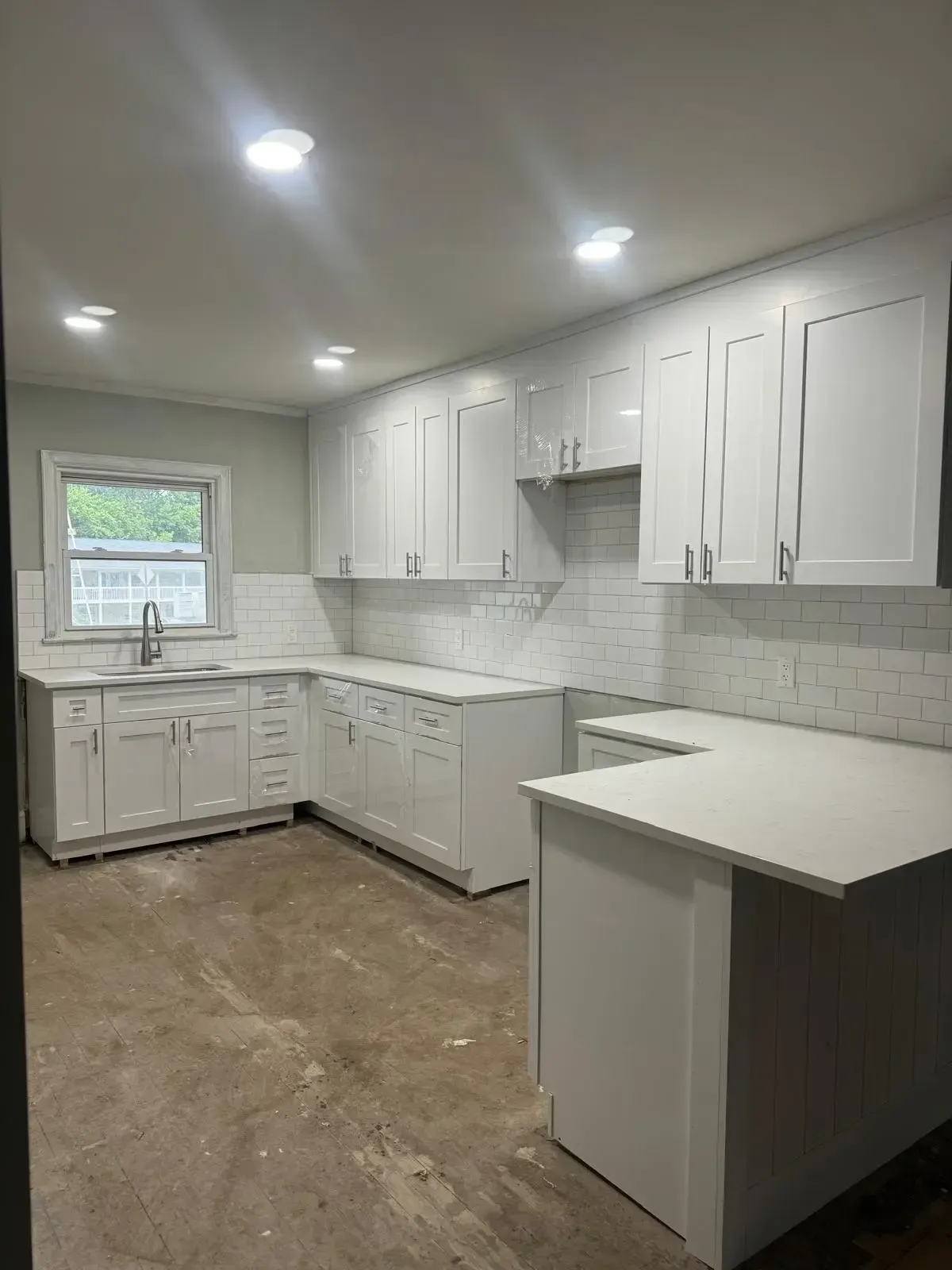 A kitchen with white cabinets , a sink , and a window.
