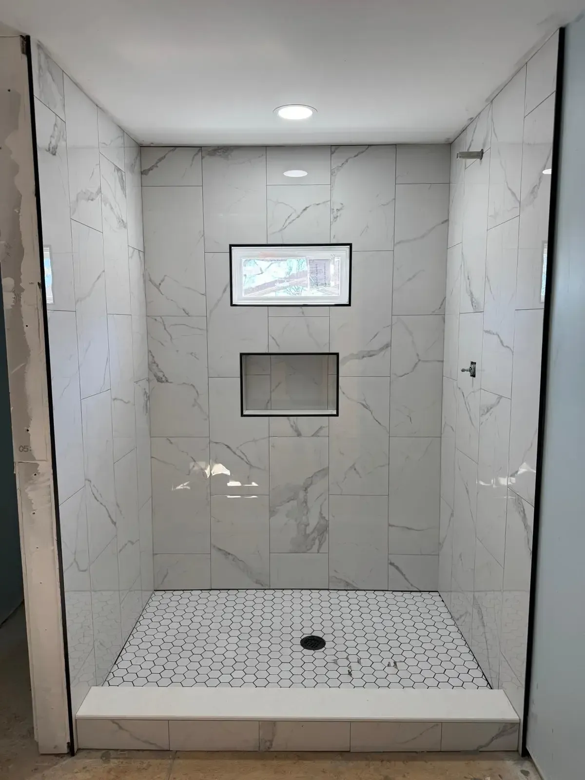 A shower stall with white tiles and a window.