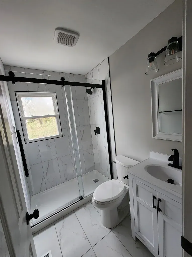A bathroom with a toilet , sink , shower and window.