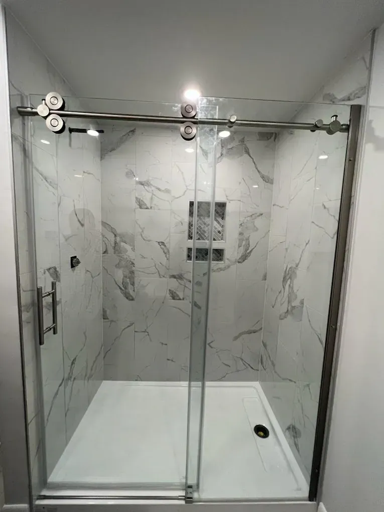 A bathroom with marble walls and a sliding glass shower door.