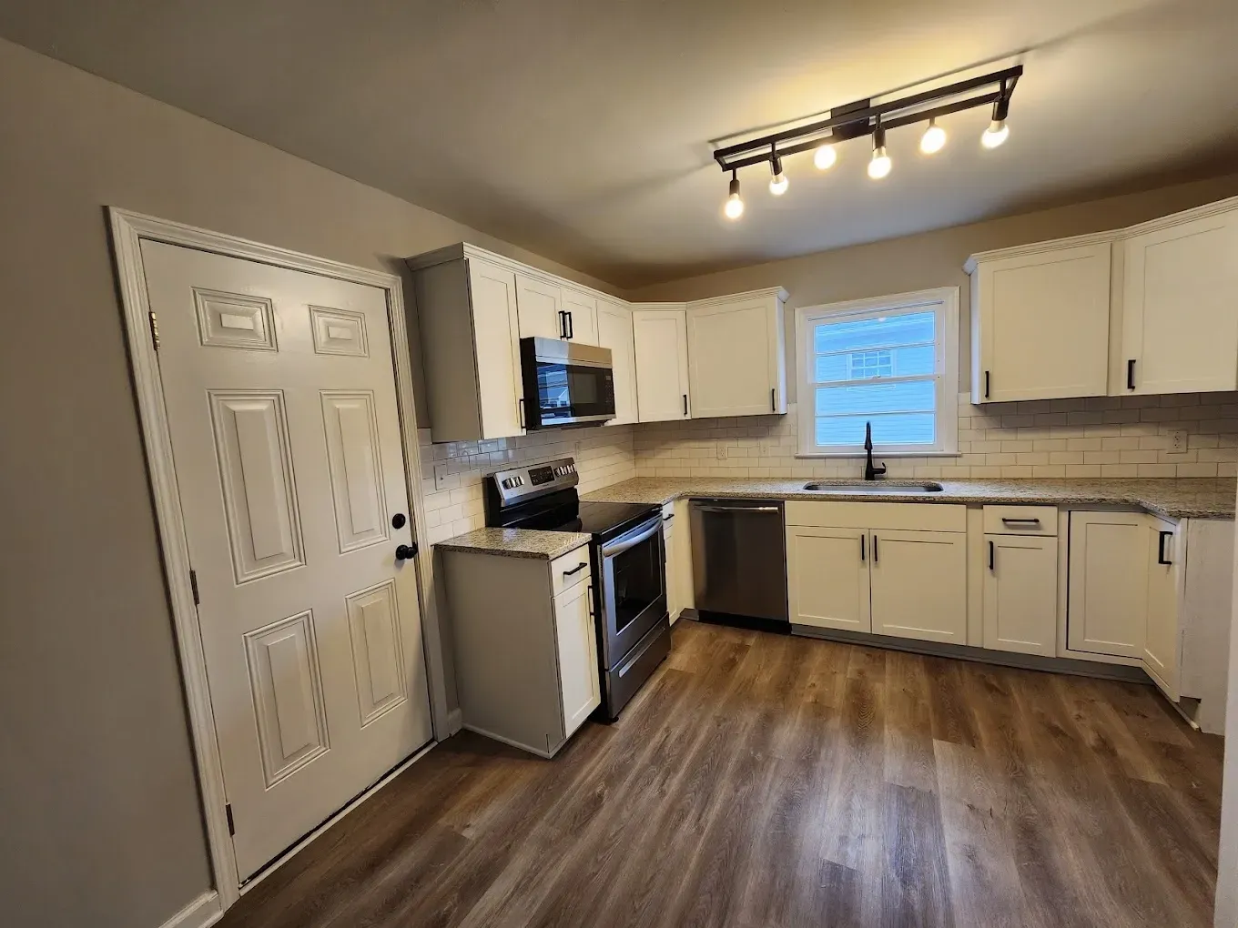 A kitchen with white cabinets , stainless steel appliances , and hardwood floors.