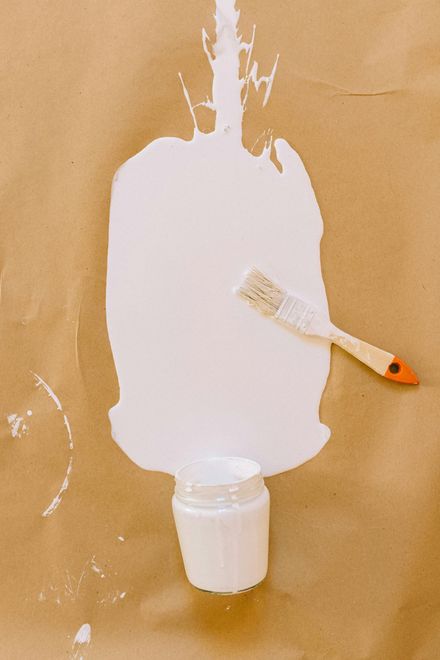 A jar of white paint and a brush on a piece of brown paper.